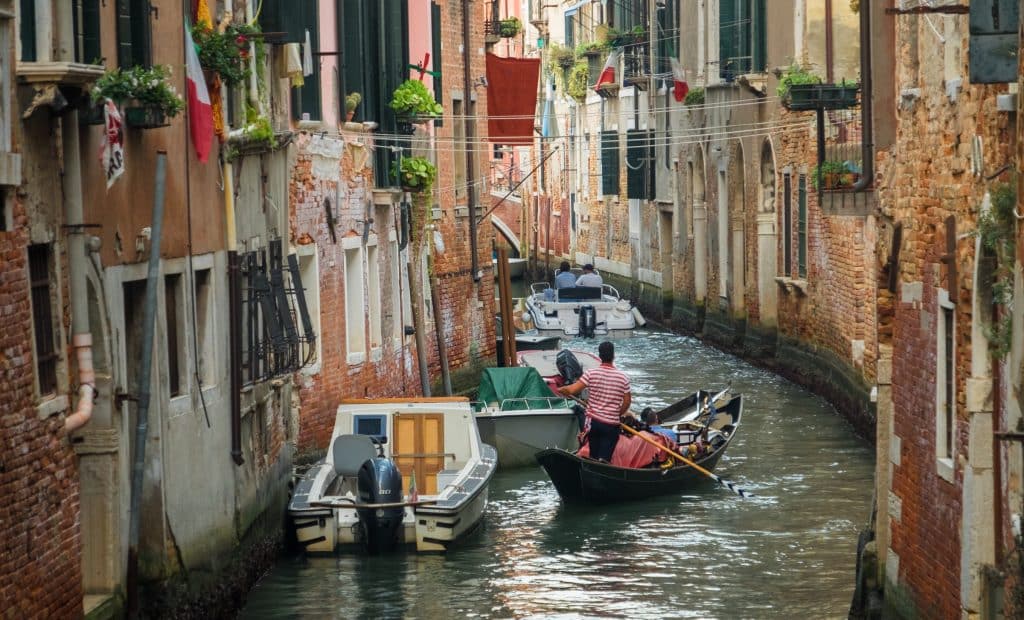 A gondolier standing in a gondola and pushing it though a quiet canal in Venice.