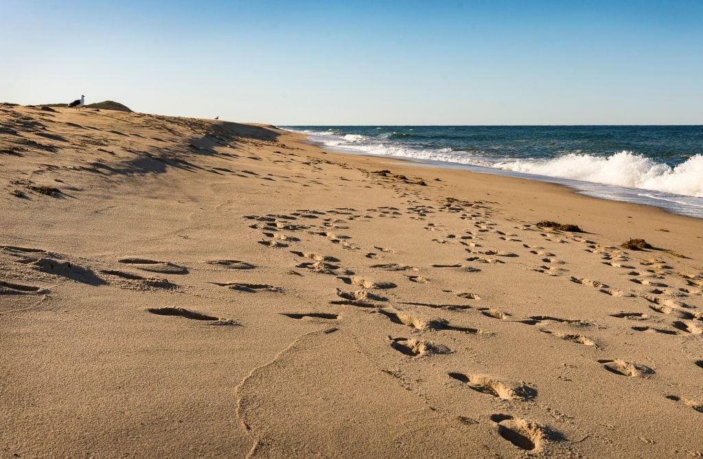 Footprints on a sandy beach as a wave crashed on the shore.