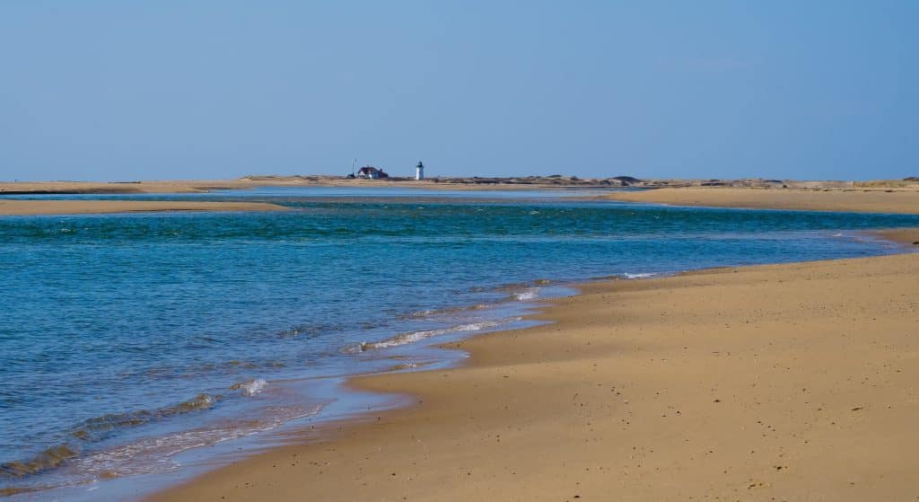 A long, smooth sandy beach on Cape Cod with a lighthouse in the distance.