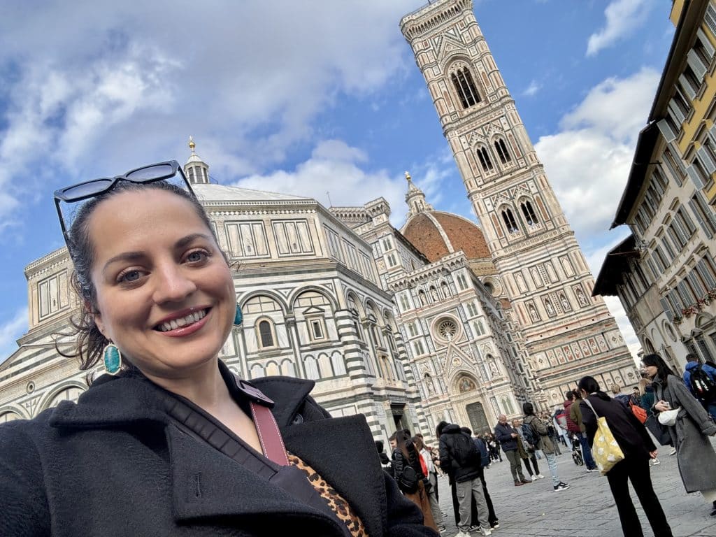 Kate smiling in front of Florence's massive white, red, and green cathedral.