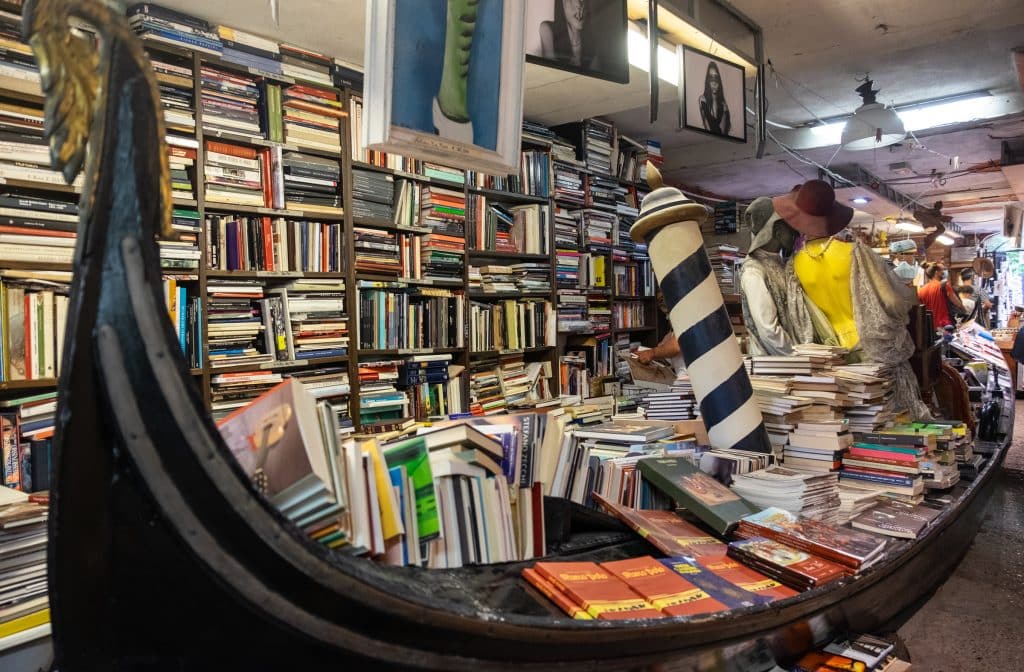A gondola filled with books in the middle of a bookstore absolutely stuffed with books from every angle.