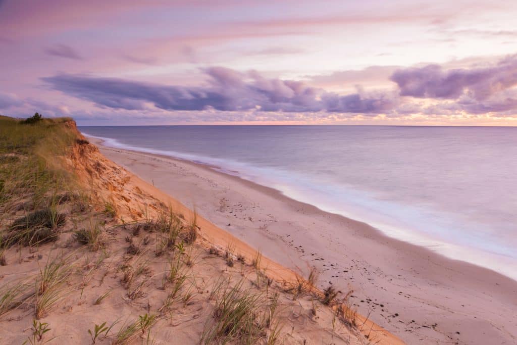 A quiet Cape Cod beach with soft sand, awash in purple sunrise light.