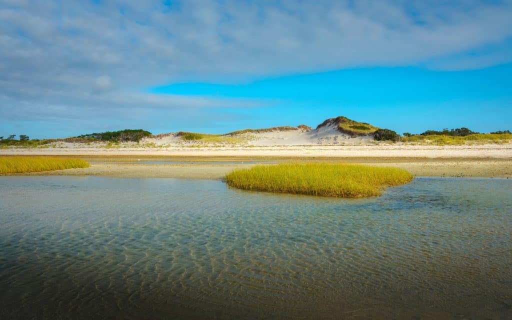A beach on Cape Cod with a calm, clear turquoise tidal pool next to the shore.