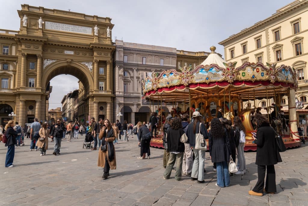 The big square of Piazza della Repubblica in Florence, with a merry-go-round sponging and lots of people walking around.