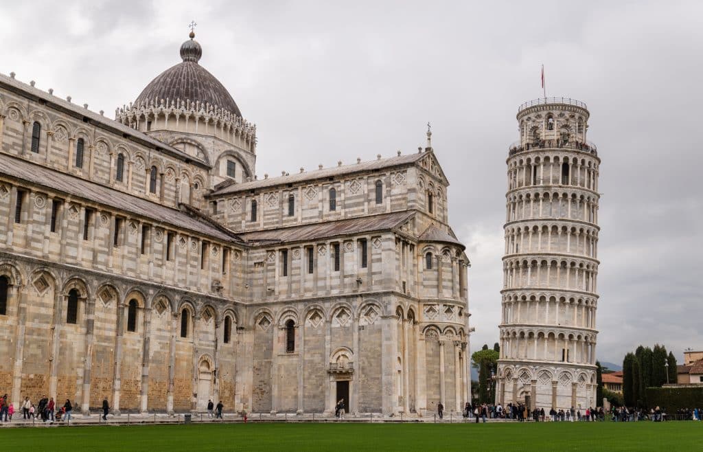 The leaning tower of Pisa, surrounded by people, on a piazza next to a big church.