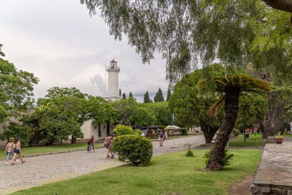 A lush green park in Colonia, with a tall white lighthouse in the background.