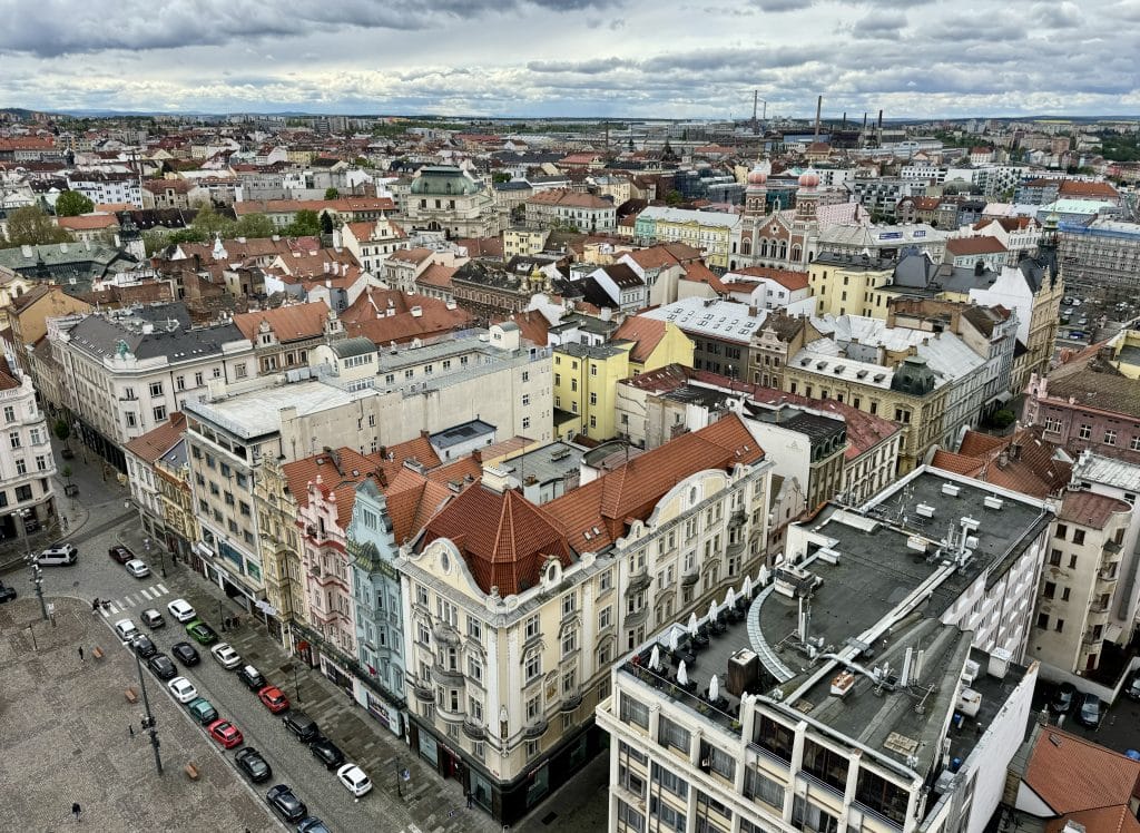 A view of the Czech city of Plzen from above: lots of pale painted crenellated buildings with red roofs, mixed in with ugly modern buildings.