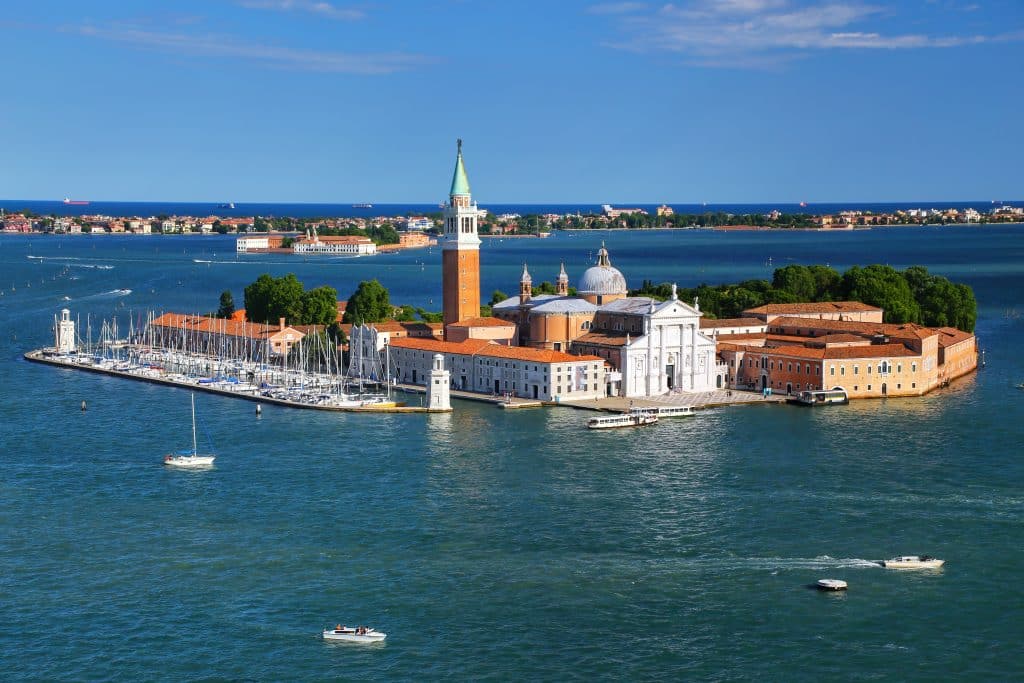 A tiny island in the Venetian lagoon, topped with a brick church tower with a white steeple.