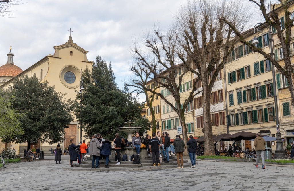 A group of teenagers hanging out at a fountain on a piazza in front of a church in Florence.