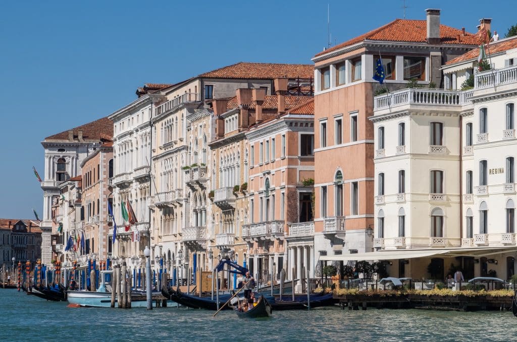 A long line of pink, white, and peach-colored buildings on the edge of a canal in Venice.