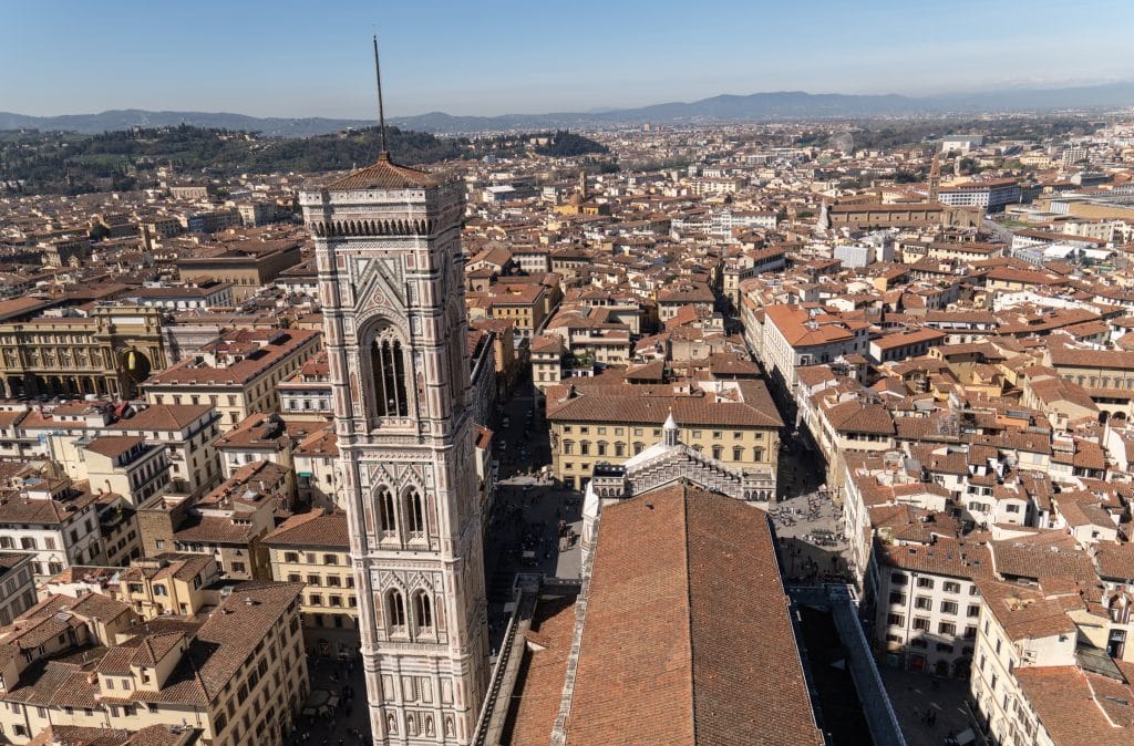 The view of Florence from the top of the Duomo, with a tall bell tower and endless buildings topped with orange roofs.