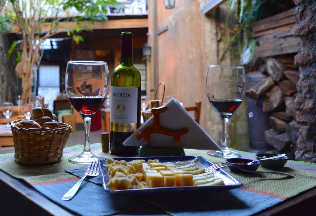 Two wine glasses in front of a plate of cheese pieces, inside a stone courtyard in Colonia.