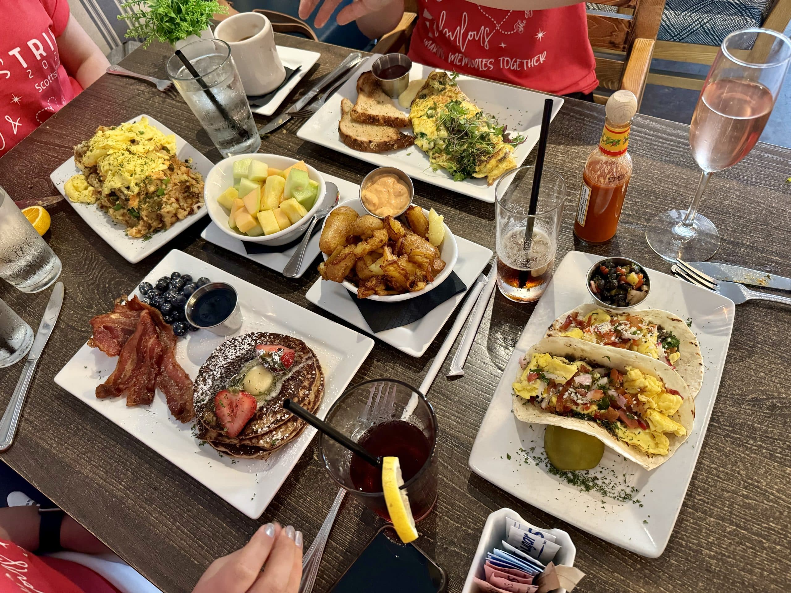 A big breakfast spread at a restaurant table with breakfast tacos, pancakes, fried potatoes, omelettes, and fruit.