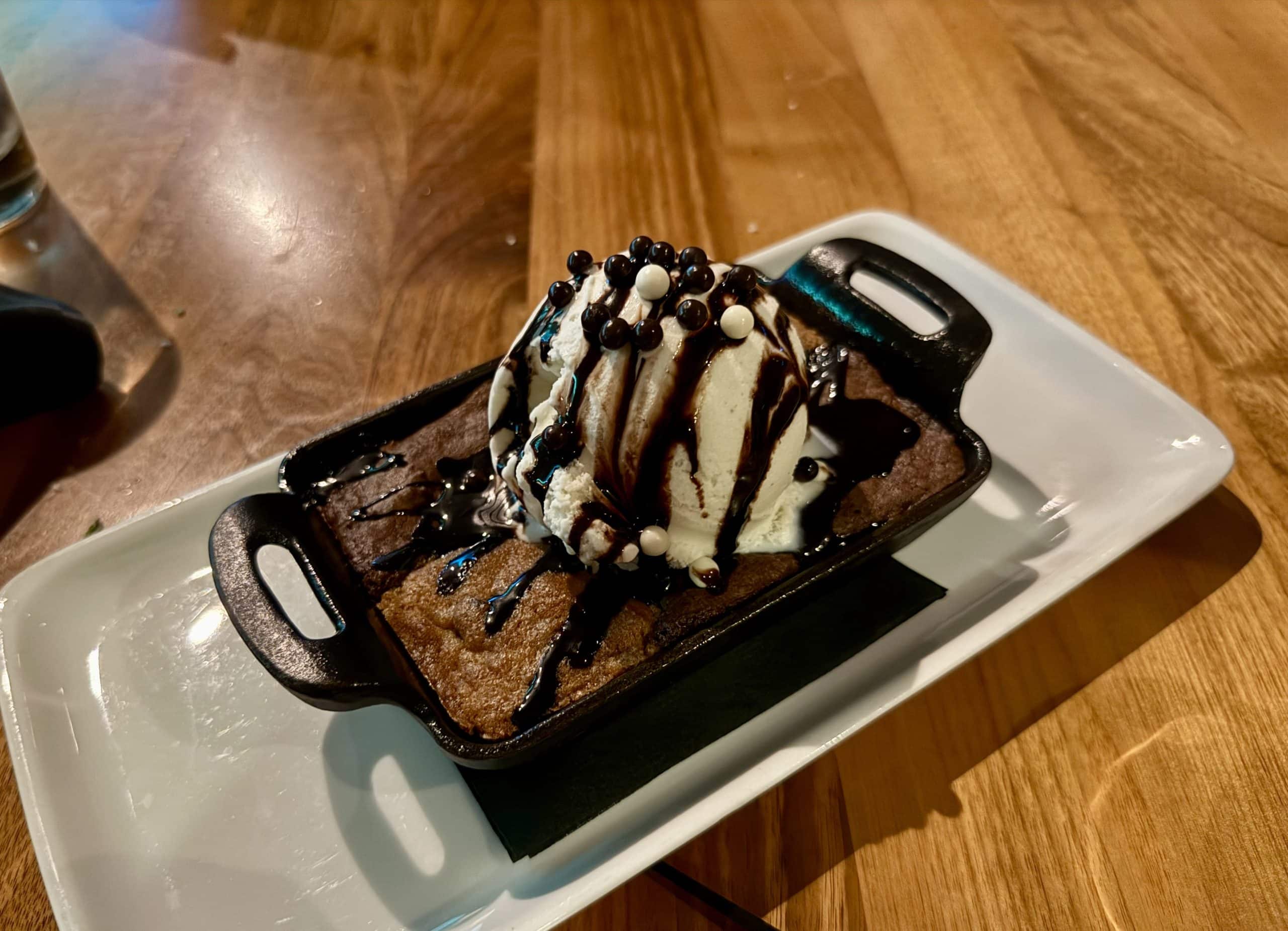 A skillet filled with a freshly cooked cookie and brownie, topped with vanilla ice cream and chocolate sauce.