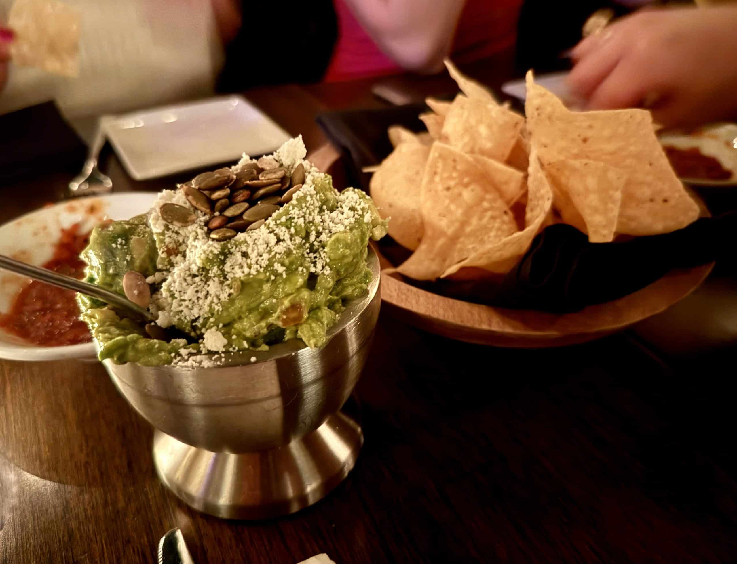 A silver bowl of guacamole next to a pile of tortilla chips.