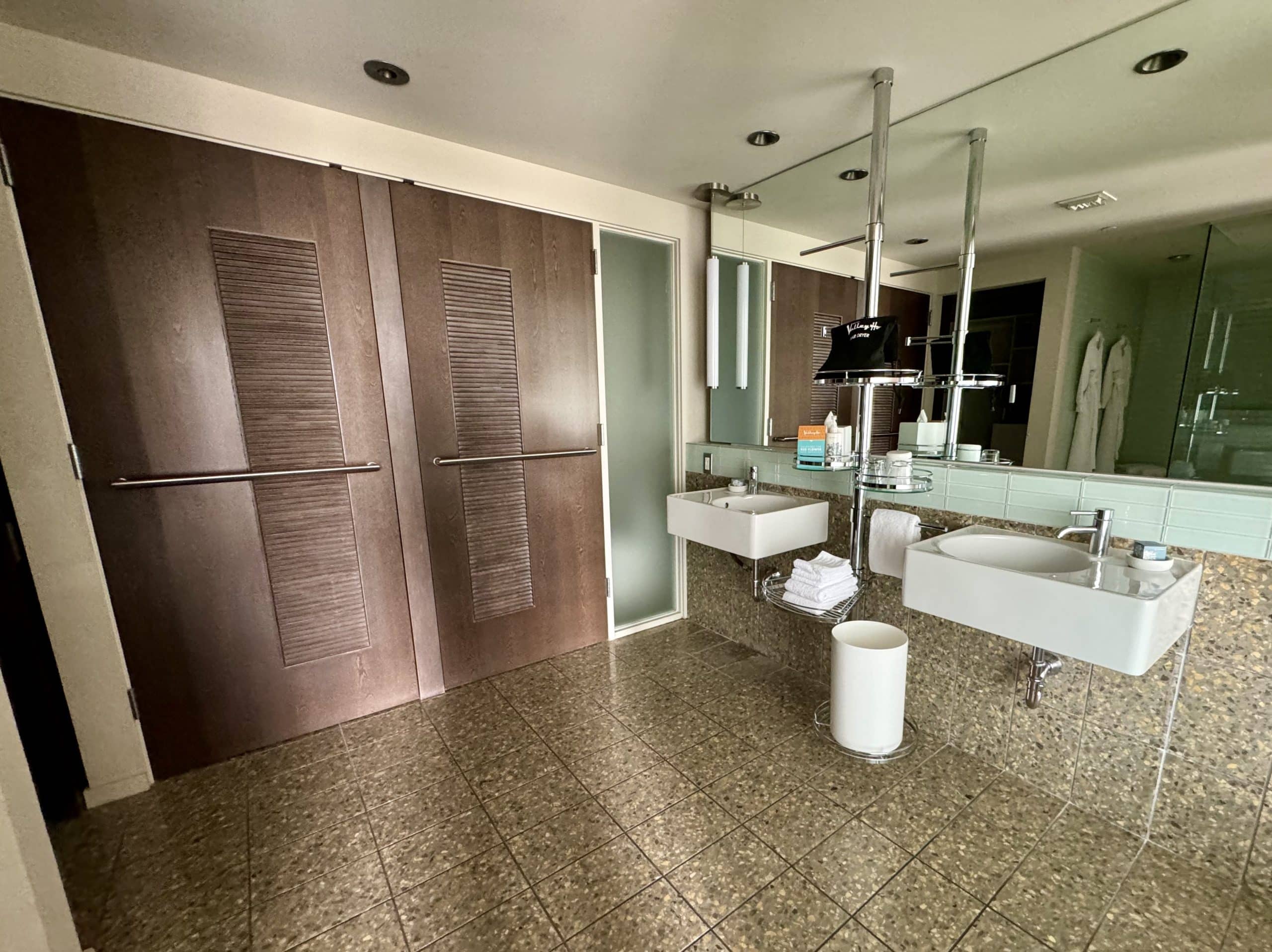 A large hotel bathroom area with two tall doors leading to a laundry nook and toilet.