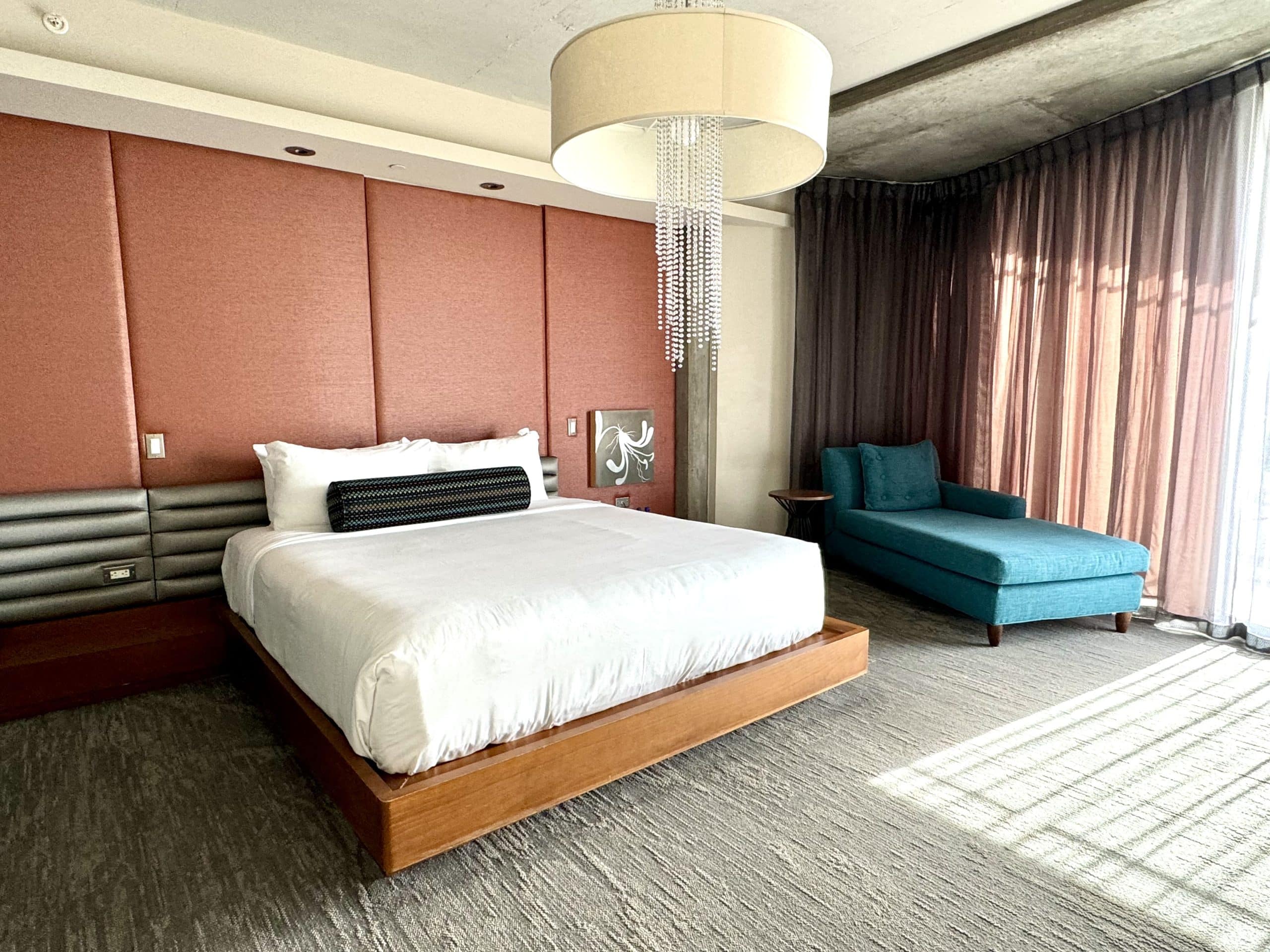A hotel room with a king-sized bed next to a teal fainting couch.