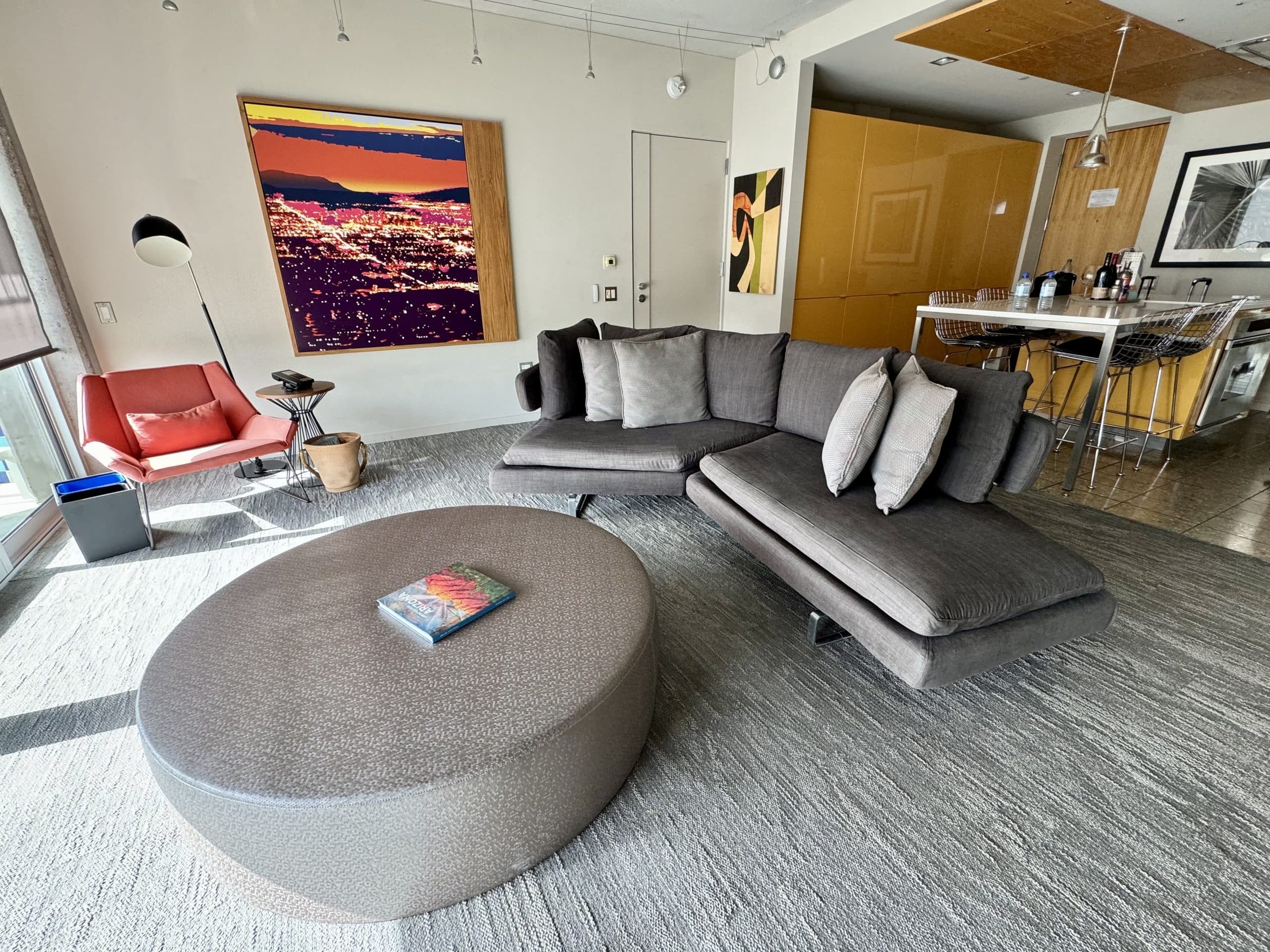 A living room area in a hotel suite with a gray couch, gray coffee table, and bright orange sitting chair.