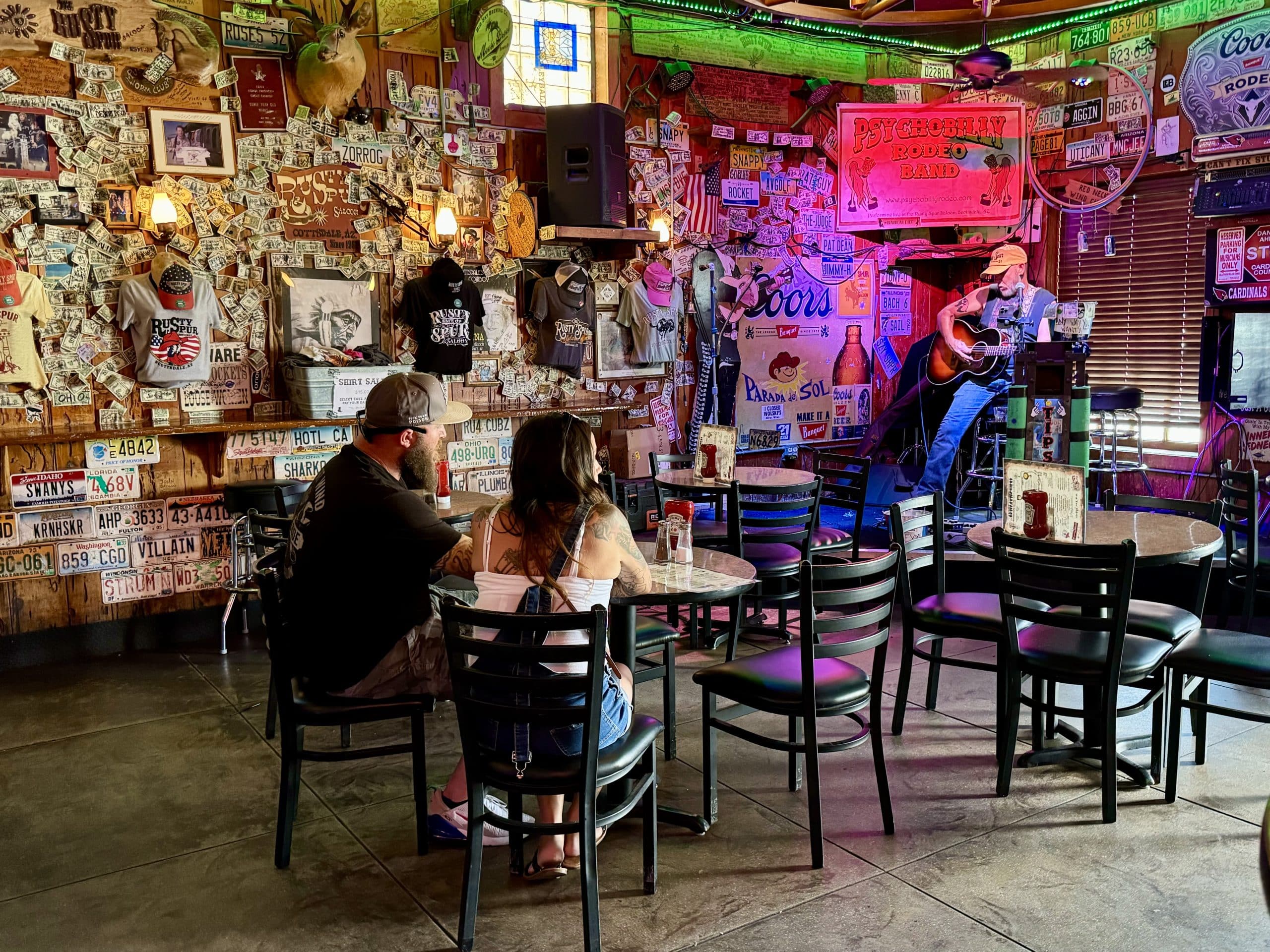 A man playing a guitar on stage in a pub, and the walls are covered with dollar bills.