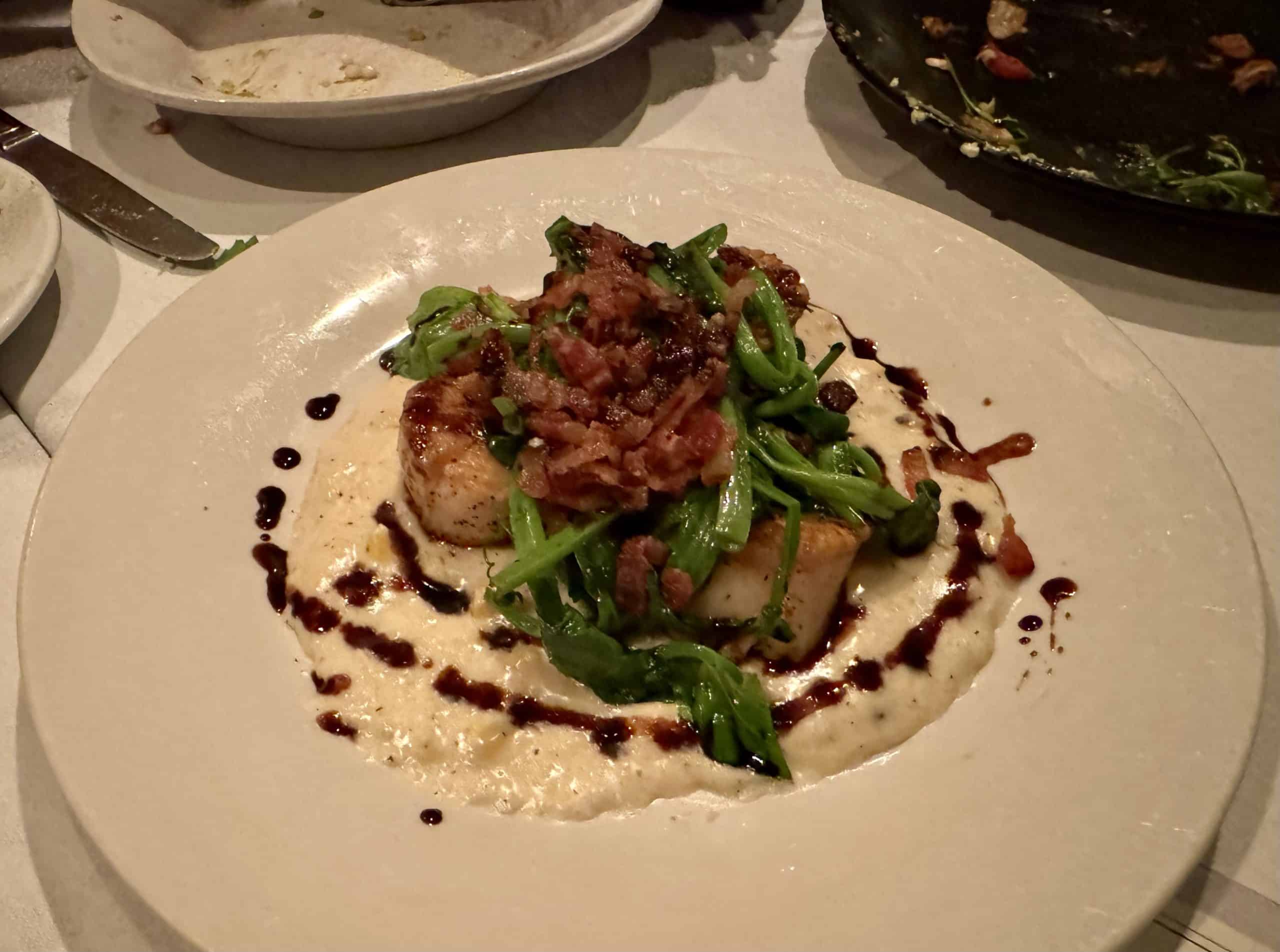 Three juicy scallops on a bed of grits, topped with bacon, greens, and balsamic vinegar.