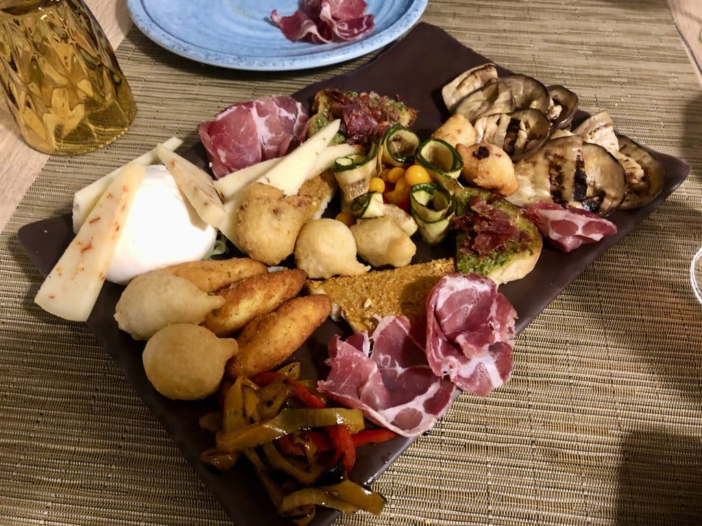 A big plate of Puglia appetizers including cured meats, roasted vegetables, cheese wedges, and various fried balls.