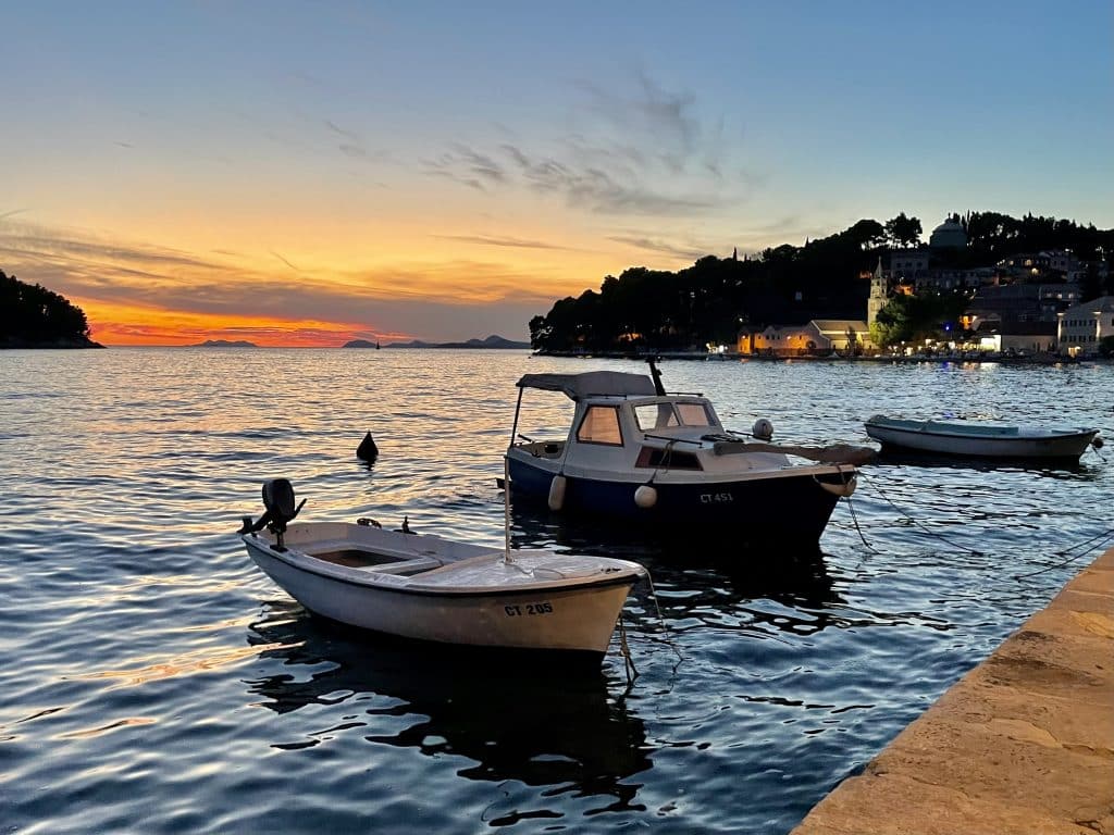 Two small boats moored near a small dock as the sun sets in the background.