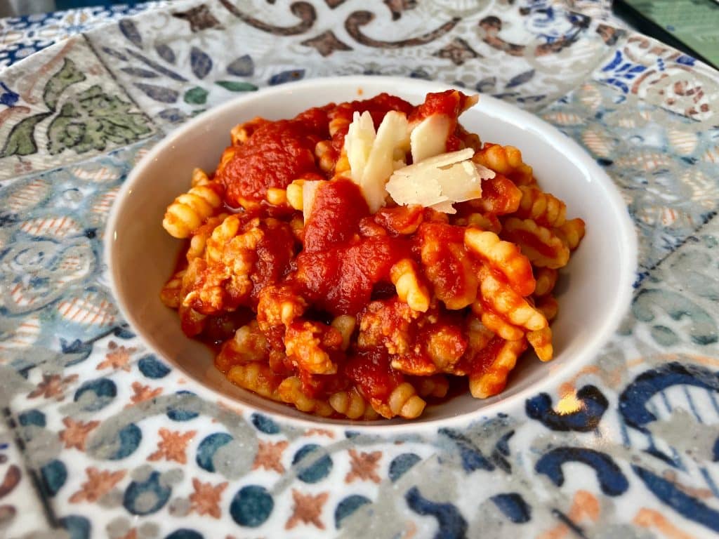 A bowl of bumpy fregola pasta in tomato sauce with a bit of cheese on top.