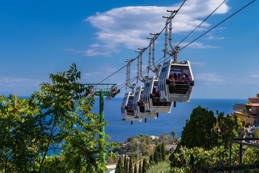 Four little cable cars in a row heading down a wire toward the sea.