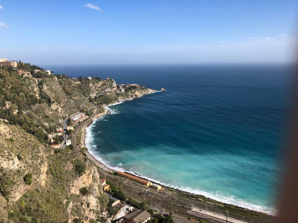 The coast of Taormina, with a train station down at the coast, next to the water.