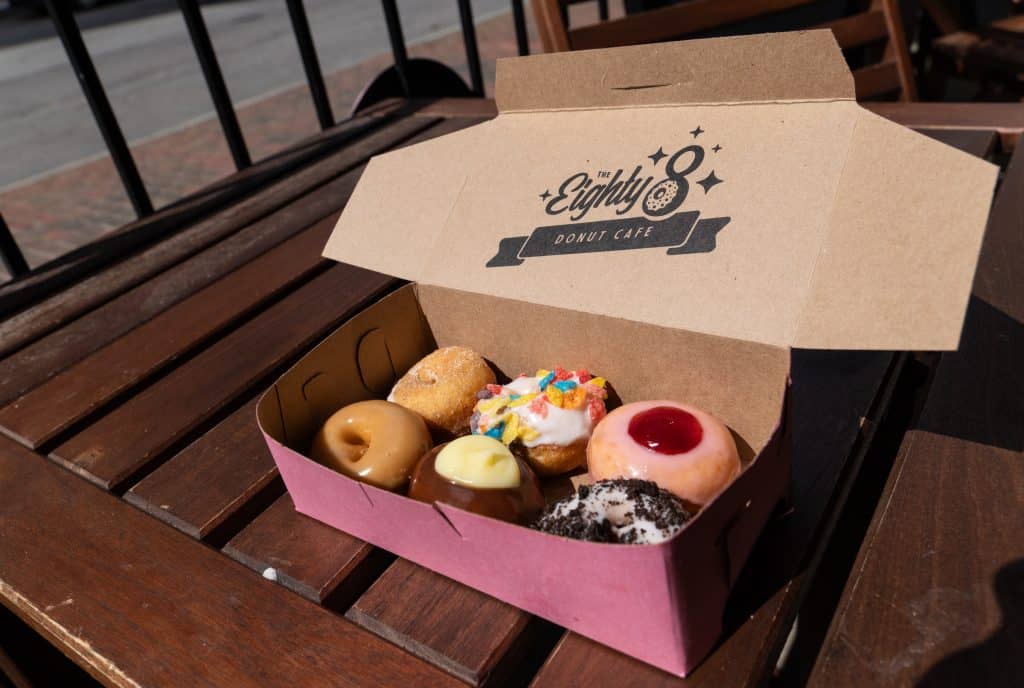 A box filled with six tiny donuts in different flavors, some covered with sprinkles or frosting.