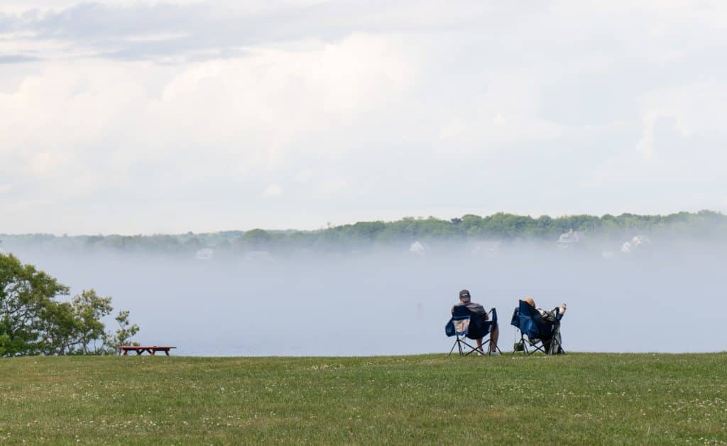 Two men sitting in camping chairs in the middle of a park as fog swirls around them.