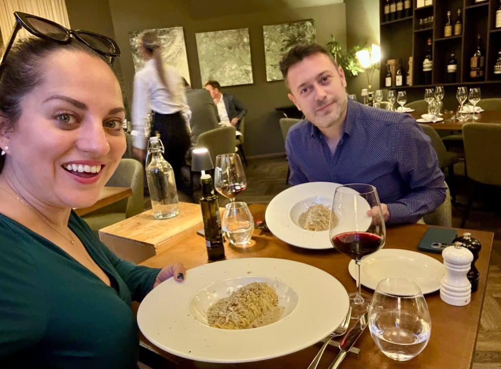 Kate and Charlie taking a selfie holding up bowls of truffle pasta.