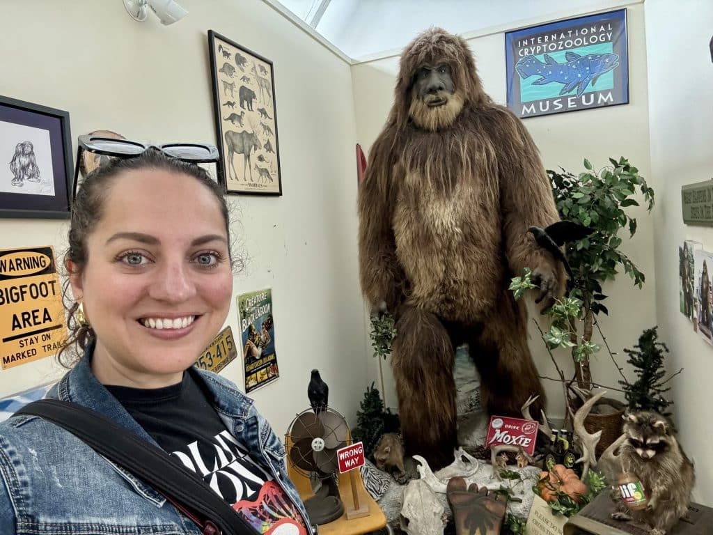 Kate taking a selfie in front of a giant Bigfoot statue with other cryptids around his feet.