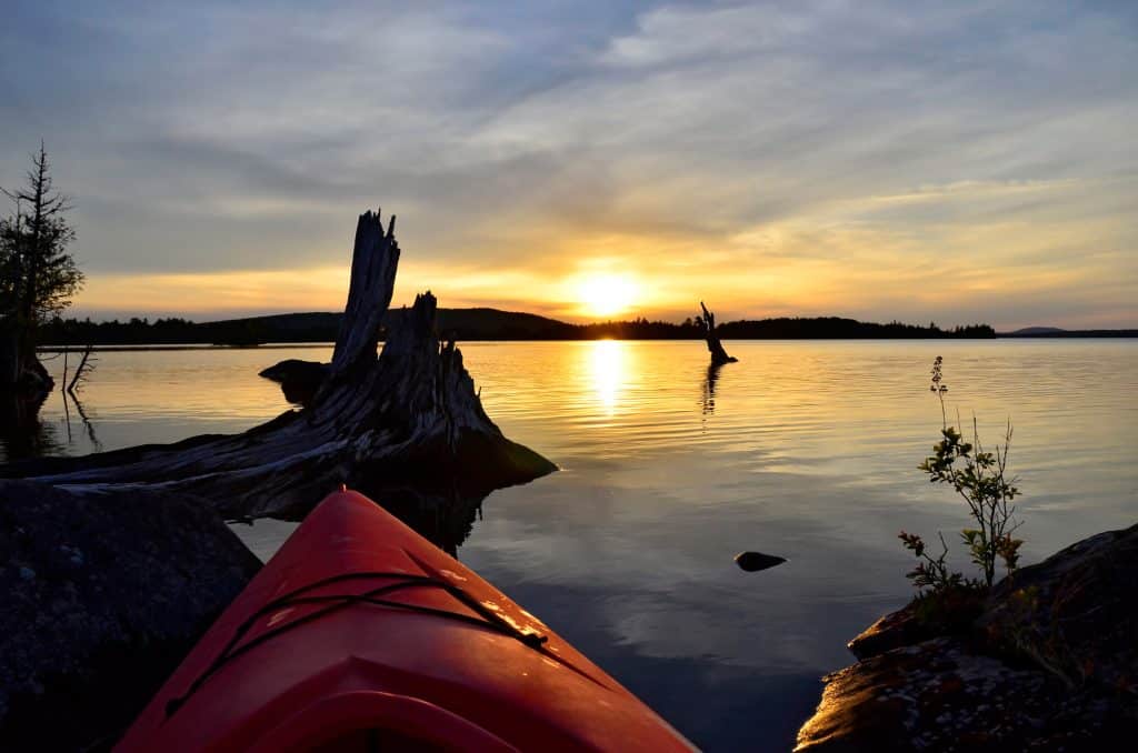 A red kayak on a still lake at sunrise.