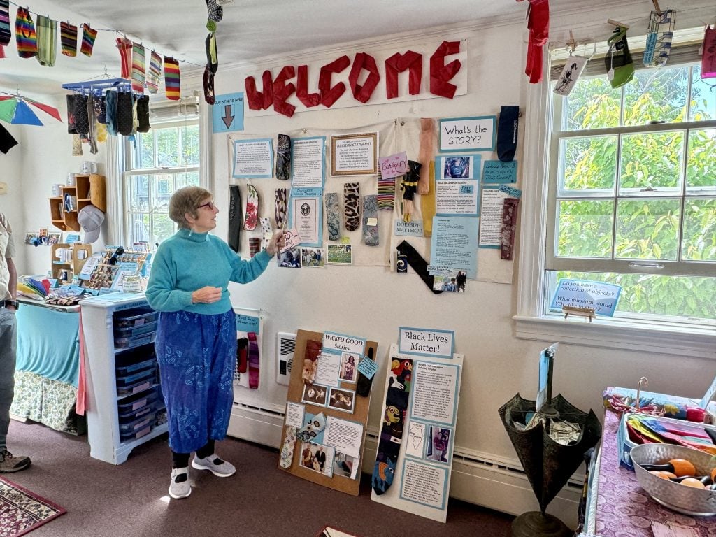 A senior woman standing in front of a display of umbrella covers, some of them forming the word "welcome."
