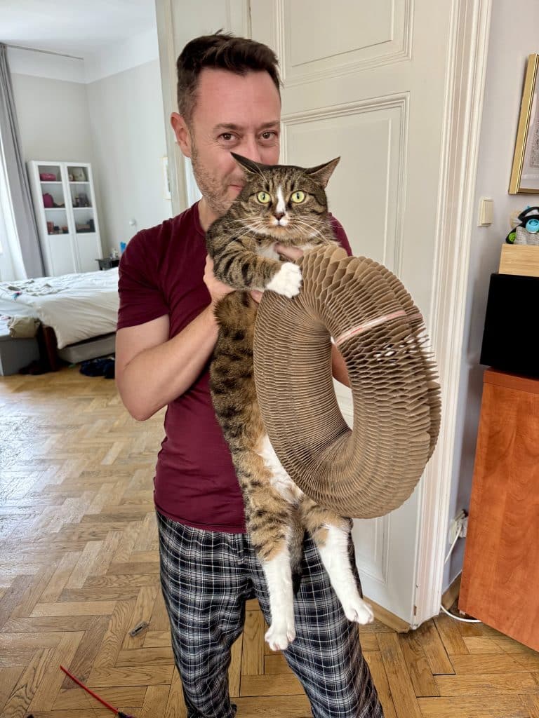 Charlie holding a wide-eyed Lewis the cat, with his claws sunken into a big cardboard ring.