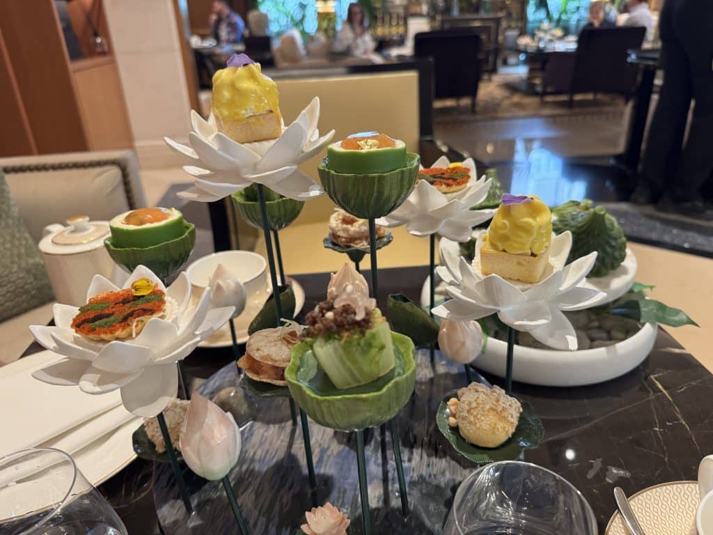 An afternoon tea set up on tiny flower and lotus-shaped dishes on stilts, looking like an upside-down chandelier.