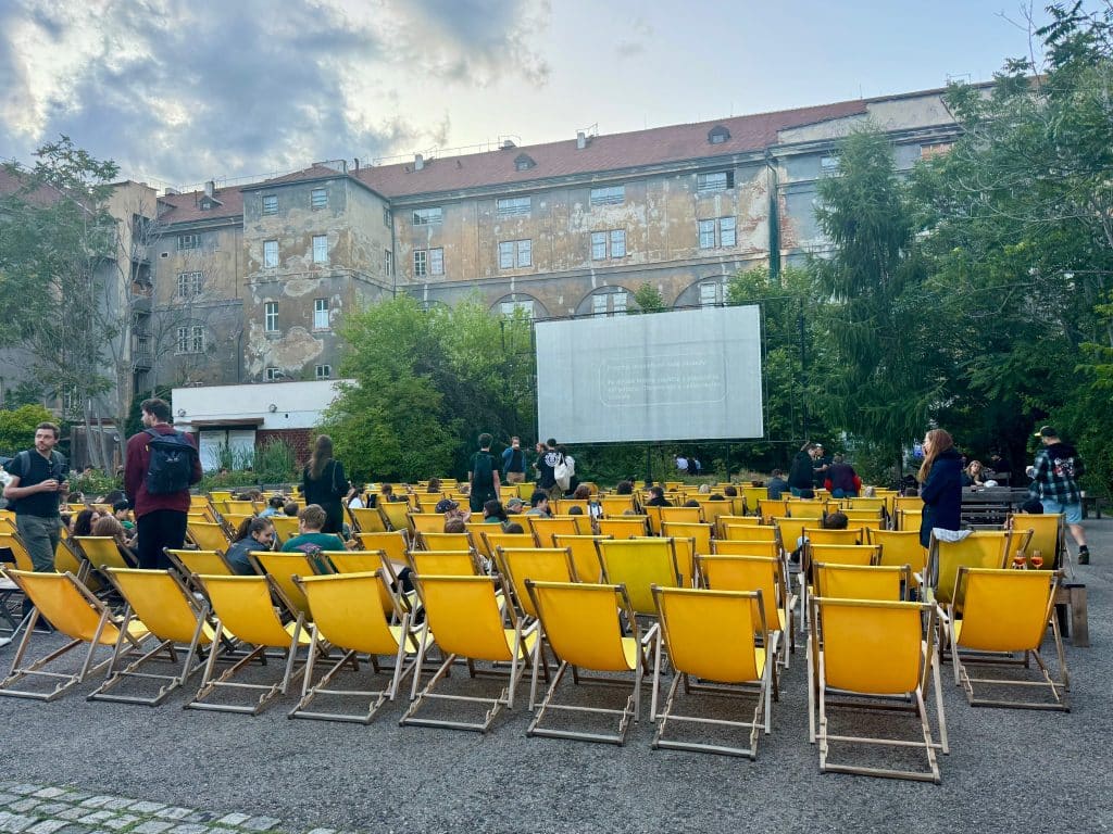 A bunch of yellow beach chairs set up in front of a big screen in a courtyard in Prague.