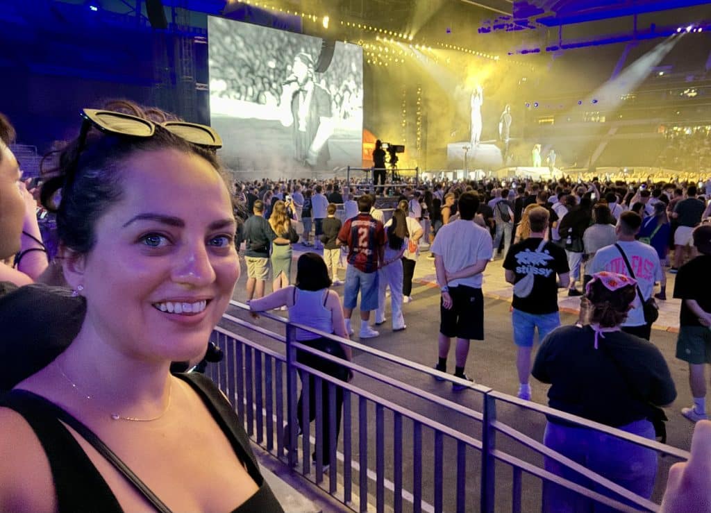 Kate taking a selfie at a concert with Kendrick Lamar and SZA on the screen and stage in the background.