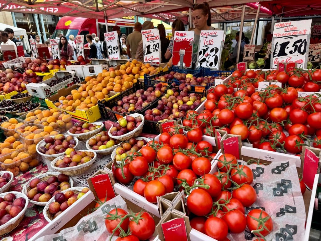 A farmer's market overflowing with bright red tomatoes, plums, and apricots.