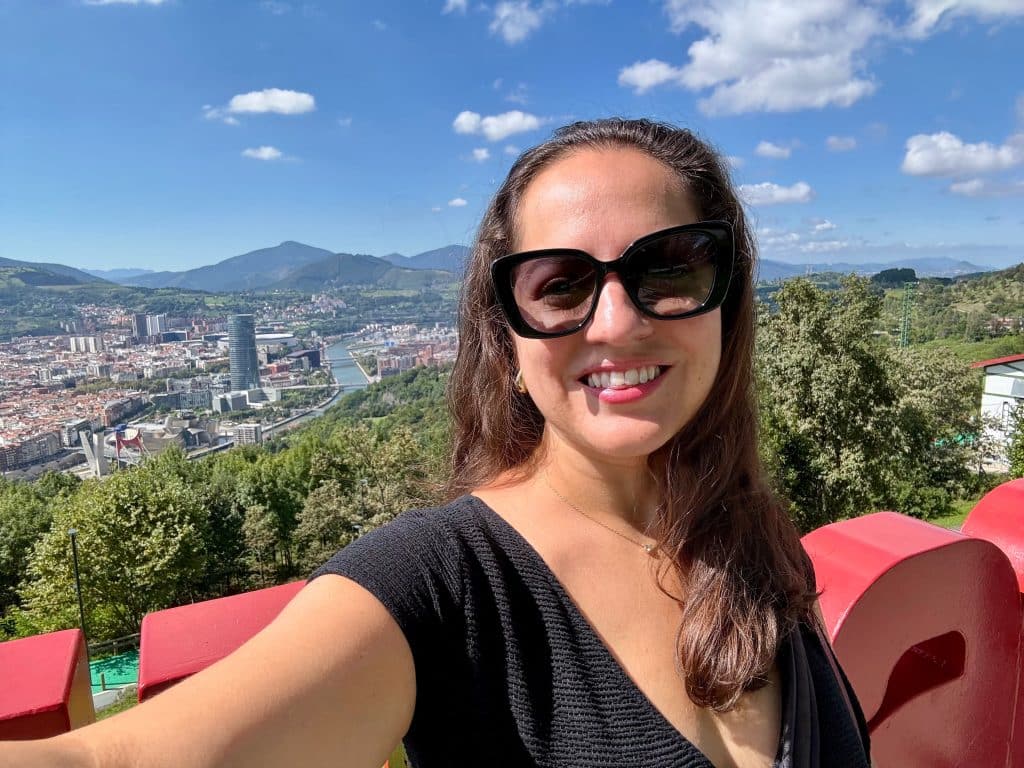 Kate taking a selfie in sunglasses with the skyline of Bilbao behind her.