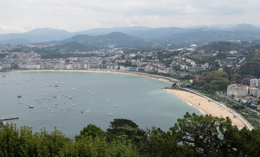 The view of the curved beach of La Concha and the city of San Sebastián from above, mountains in the background.