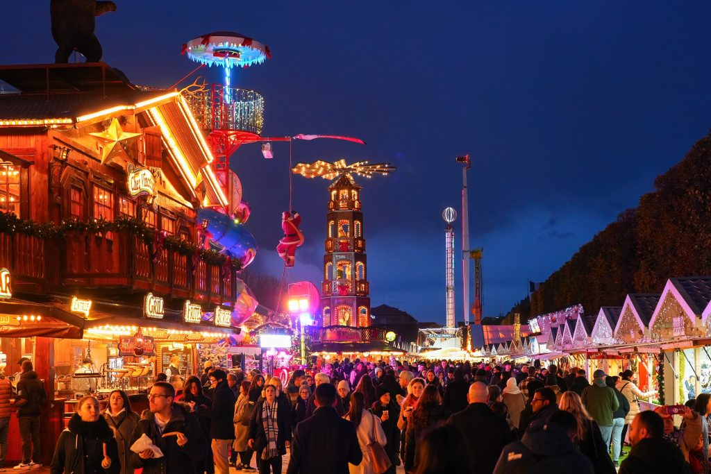 A Christmas market in Paris with German-styled half-timbered booths and a large wooden carousel in the background.