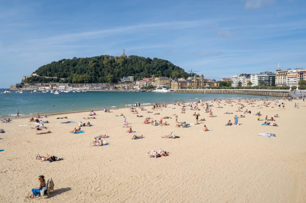A wide, sandy beach with calm blue water and lots of people sunbathing.