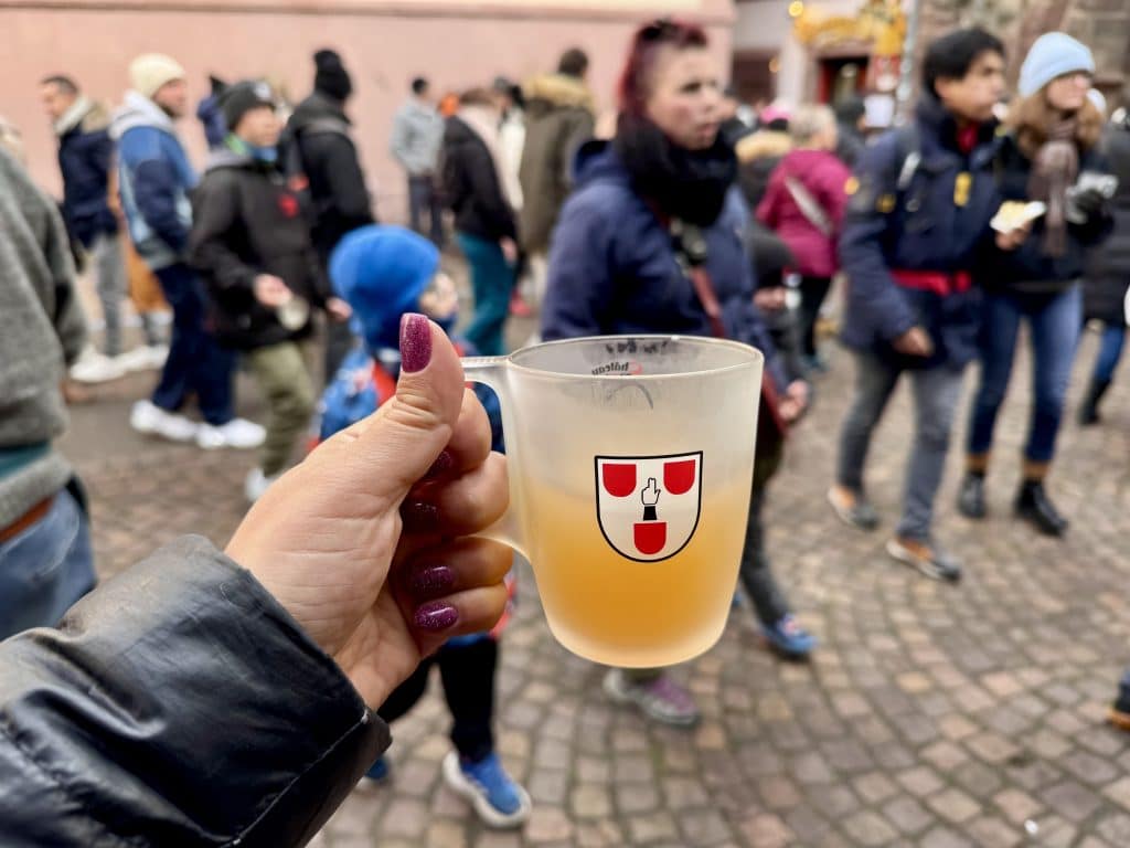 A hand holding up a frosted glass of apple cider with a medieval crest on it.