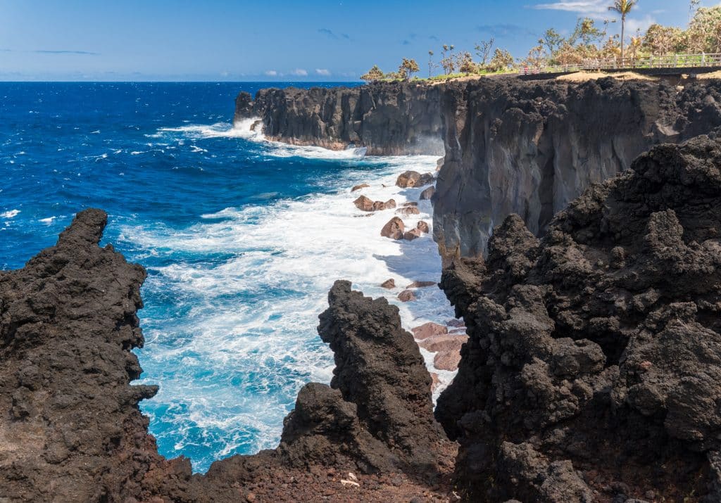 Black volcanic cliffs and crashing white waves in the blue sea below.