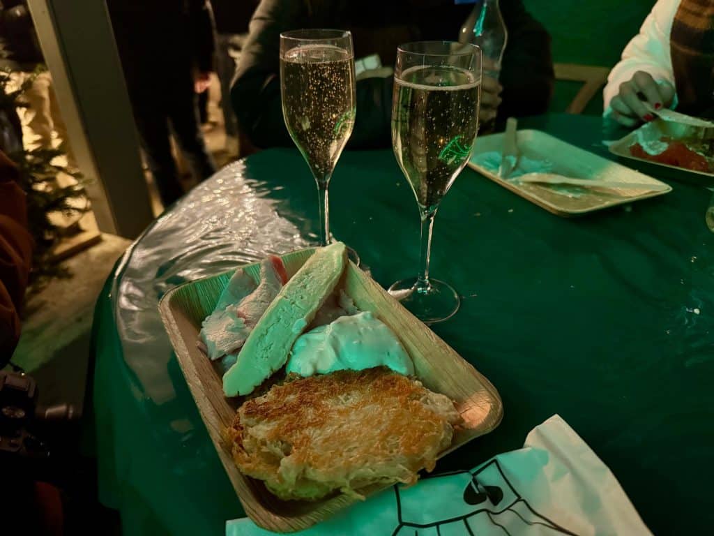 Two glasses of champagne and a tasting plate with potato pancakes and several cheeses.