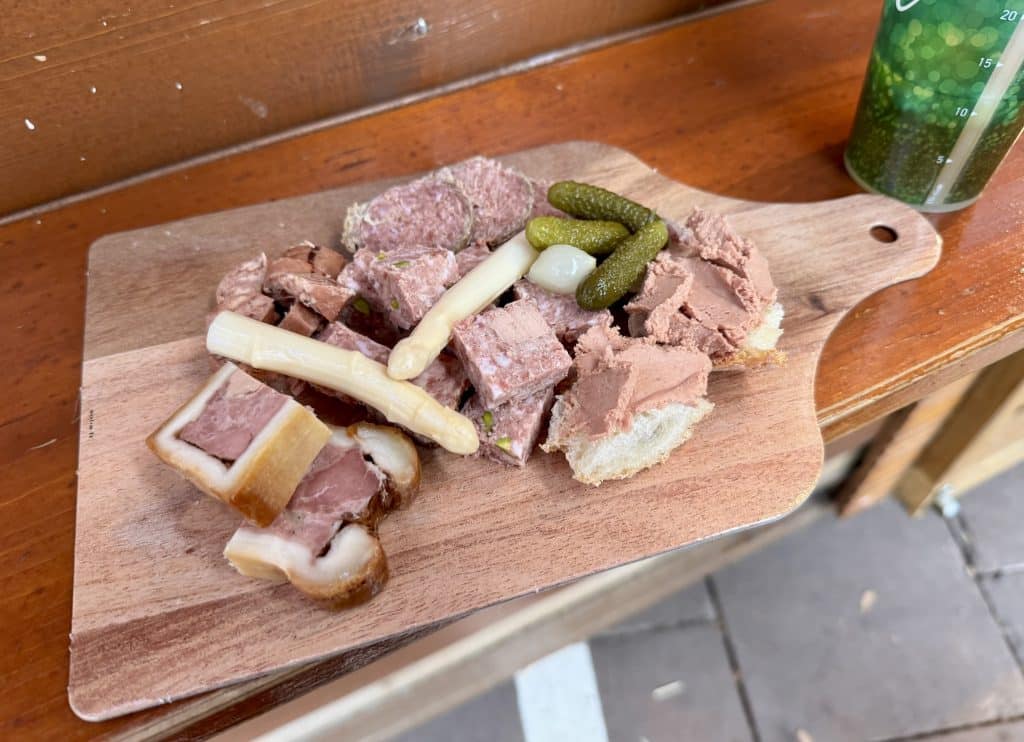 A wooden board filled with many kinds of charcuterie and pickles.