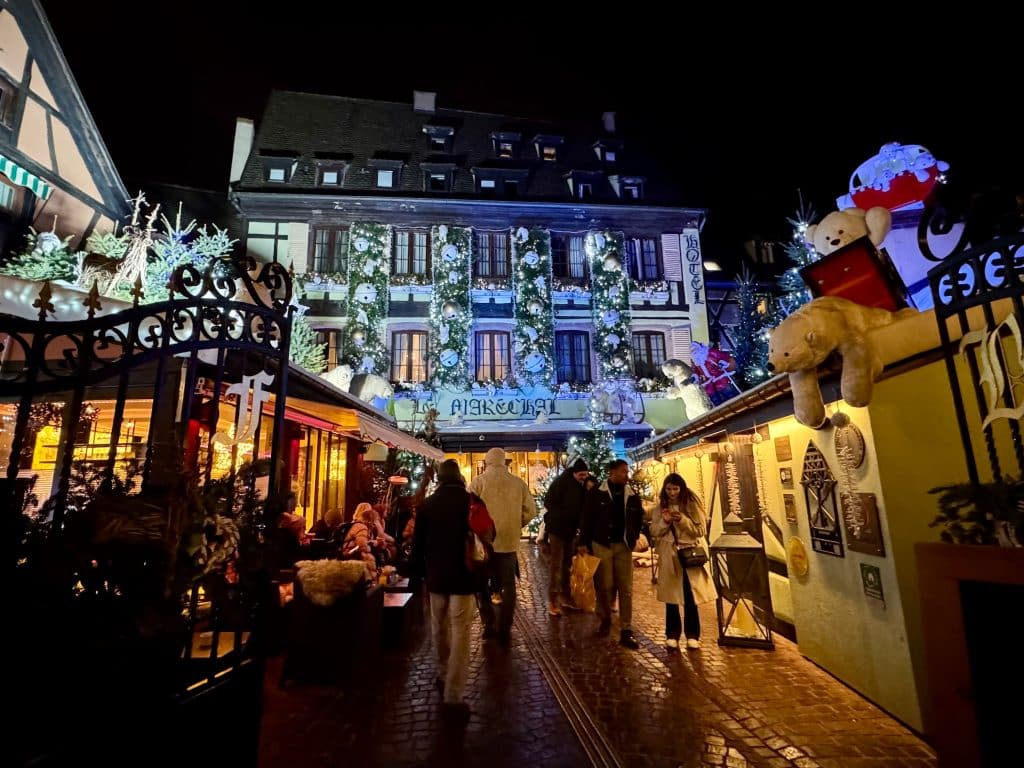 Beautiful half-timbered buildings in Colmar after dark, covered with twinkling Christmas lights and decorations.