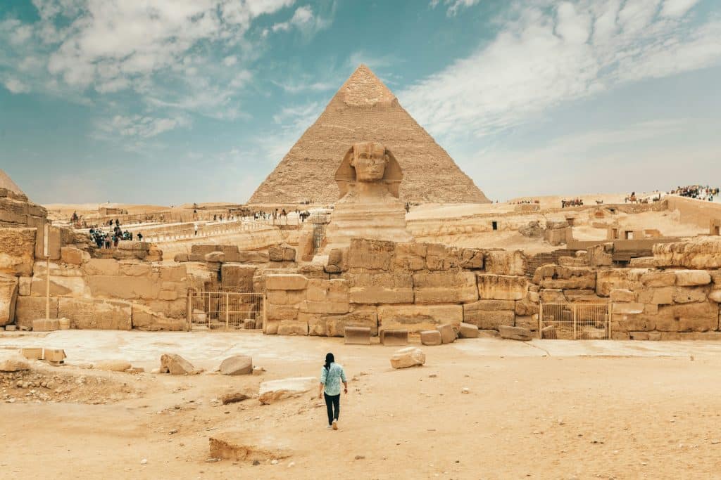 A woman walking towards the Great Sphinx and a pyramid in Egypt.
